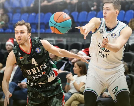 Двое баскетболистов в динамичной борьбе за мяч на площадке. Игрок в форме тёмного камуфляжа противостоит спортсмену в белой форме. На заднем плане зрители на трибунах