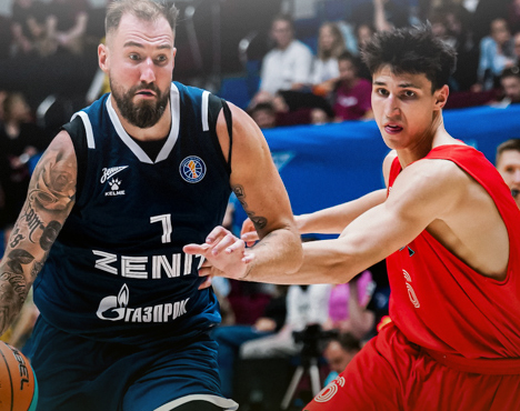 На изображении два баскетболиста в игровом моменте. Игрок в тёмно-синей форме с мячом обходит соперника в красной форме. На заднем плане видна аудитория зрителей