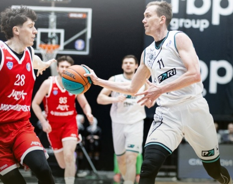 На изображении запечатлен момент баскетбольного матча. Игрок в белой форме с мячом обходит соперников в красной форме. Динамичная спортивная игра на волейбольной площадке